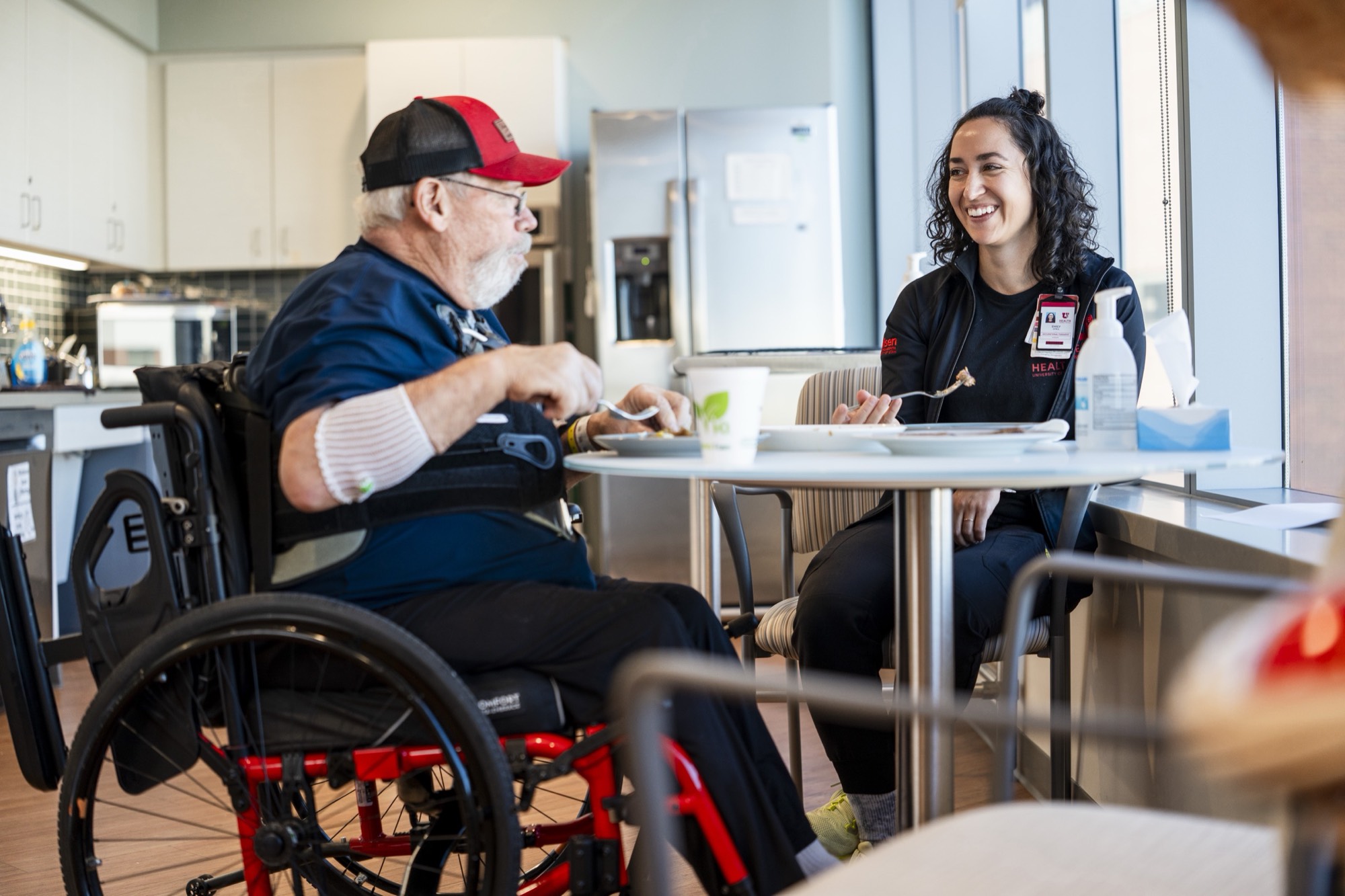 A person in a wheelchair talking with a caregiver at a kitchen table